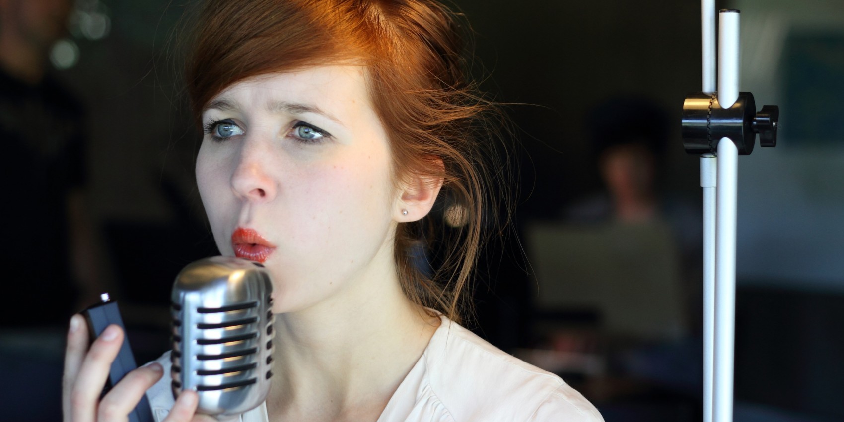 A woman sings, mouth pursed, into a silver microphone