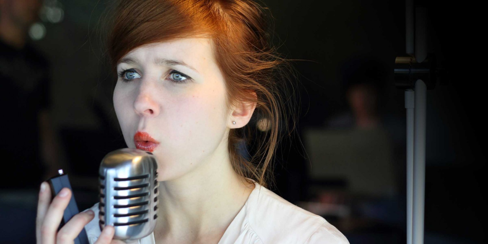 A woman sings, mouth pursed, into a silver microphone