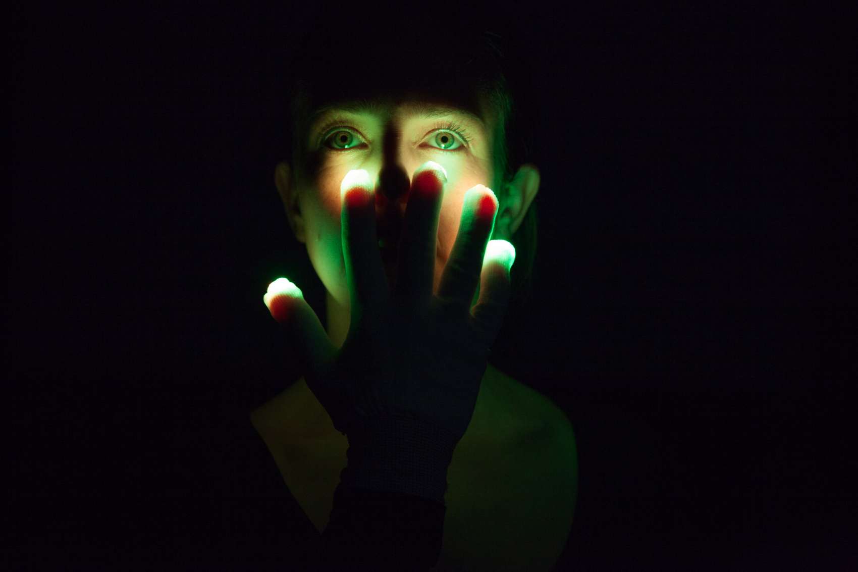A woman holding her hand in front of her illuminated face against a dark background