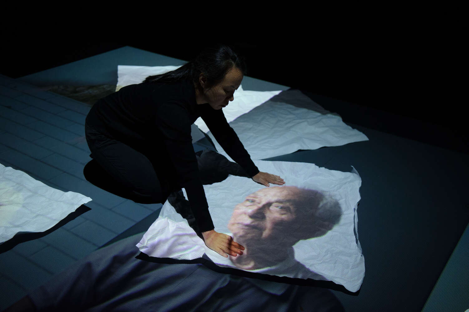 A woman leans over an image of a man projected onto paper